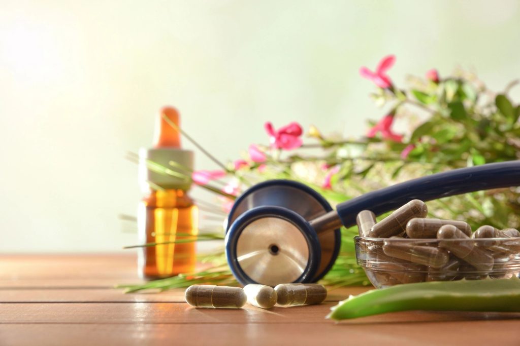 Natural herbal medicine capsules on wood table with stethoscope plants and bottle with medicinal liquid and green background.