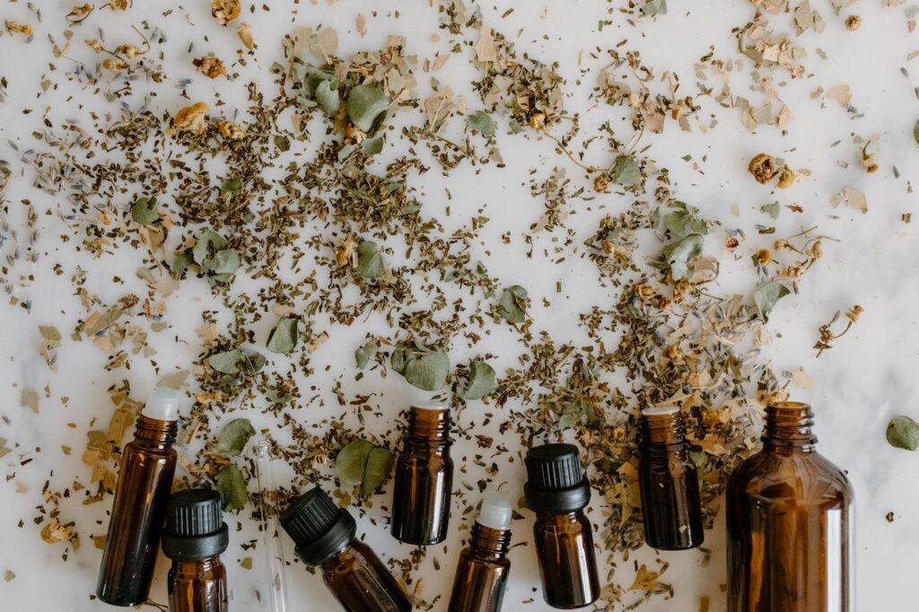 pexels-photo-6694191 Glass bottles with essential oils surrounded by scattered dried herbs on a white surface.