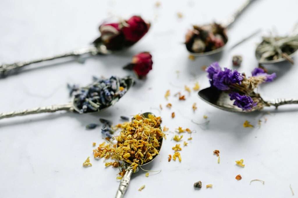 A detailed shot of various dried flowers on ornate spoons on a marble surface.