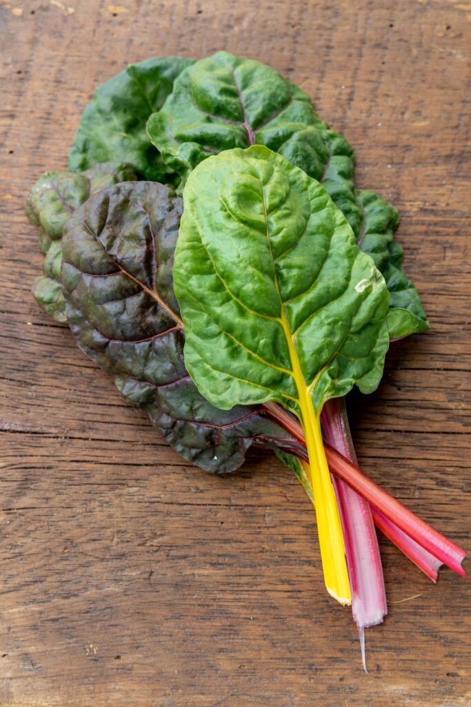 Vibrant fresh Swiss chard leaves with colorful stalks on a rustic wooden table.