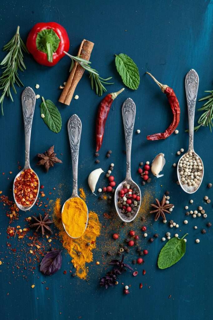 A vibrant flat lay of assorted spices on a blue surface with spoons and herbs.