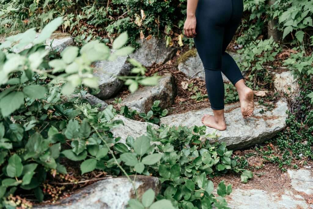 pexels-photo-8981001-8981001 Adult walking barefoot on a rocky path surrounded by greenery, embracing nature's connection.